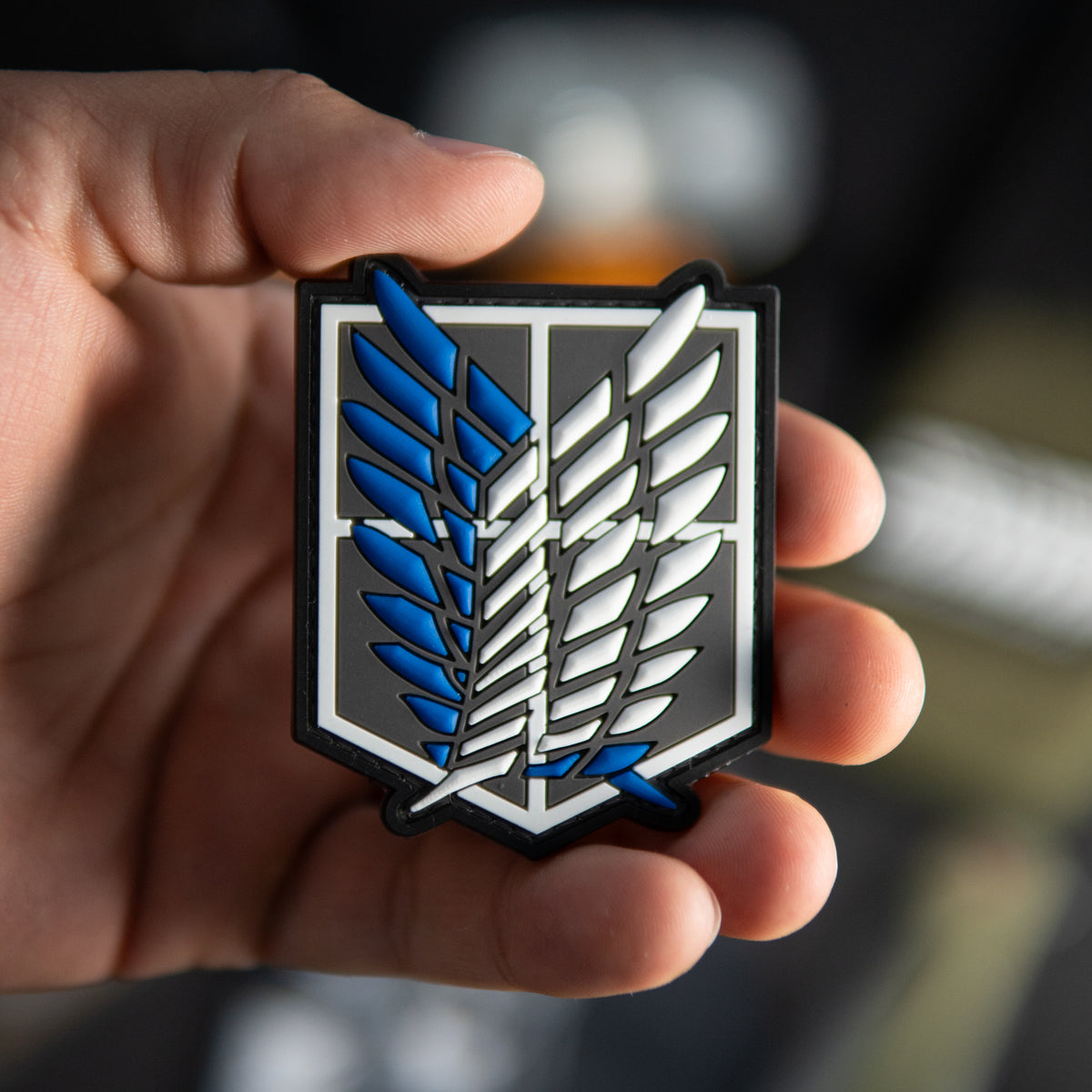 Close-up of Attack on Titan PVC morale patch with blue and white winged emblem held in a hand
