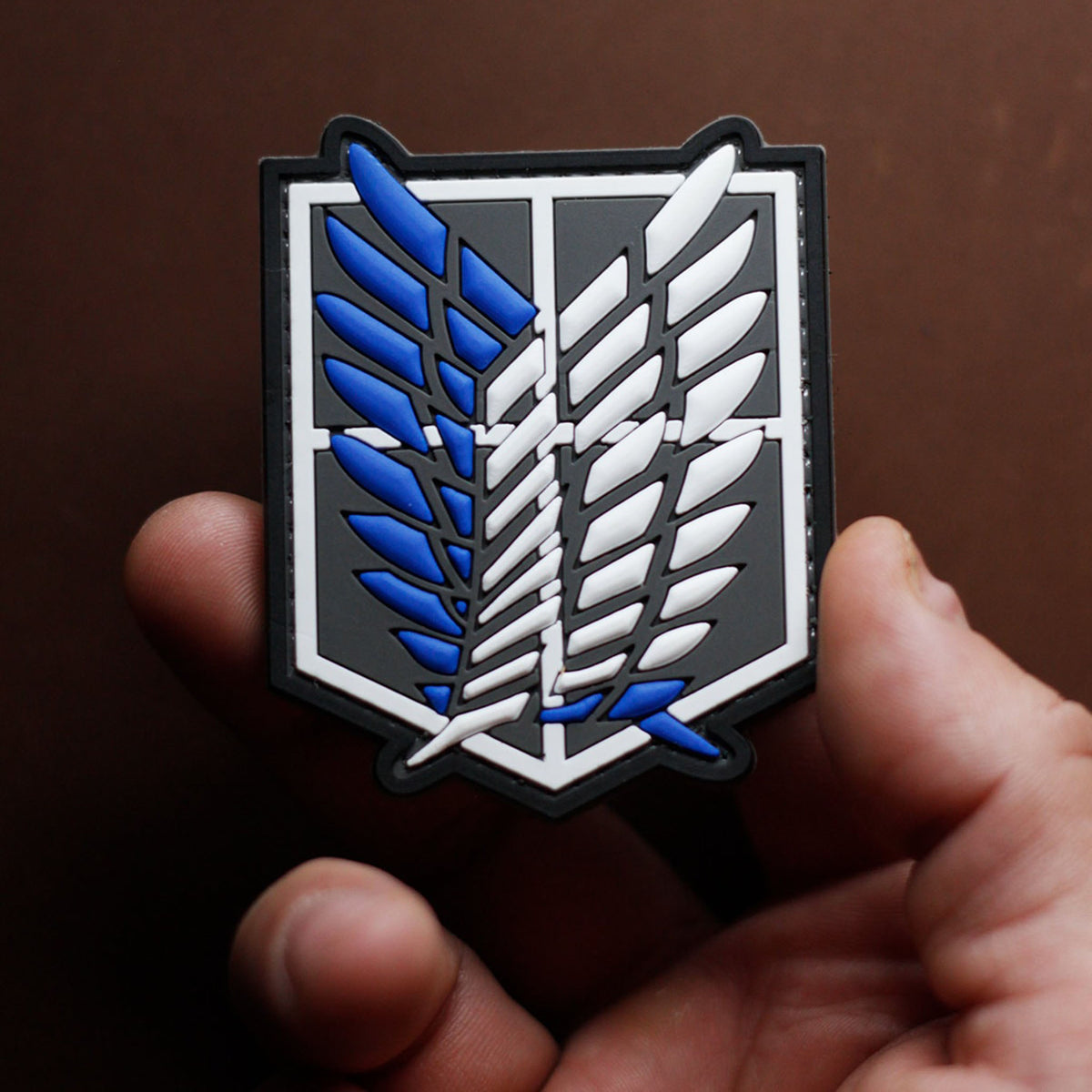Attack on Titan PVC morale patch with blue and white winged emblem held in a han