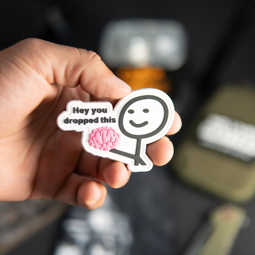 Hey You Dropped This PVC morale patch with pink brain design held in a hand