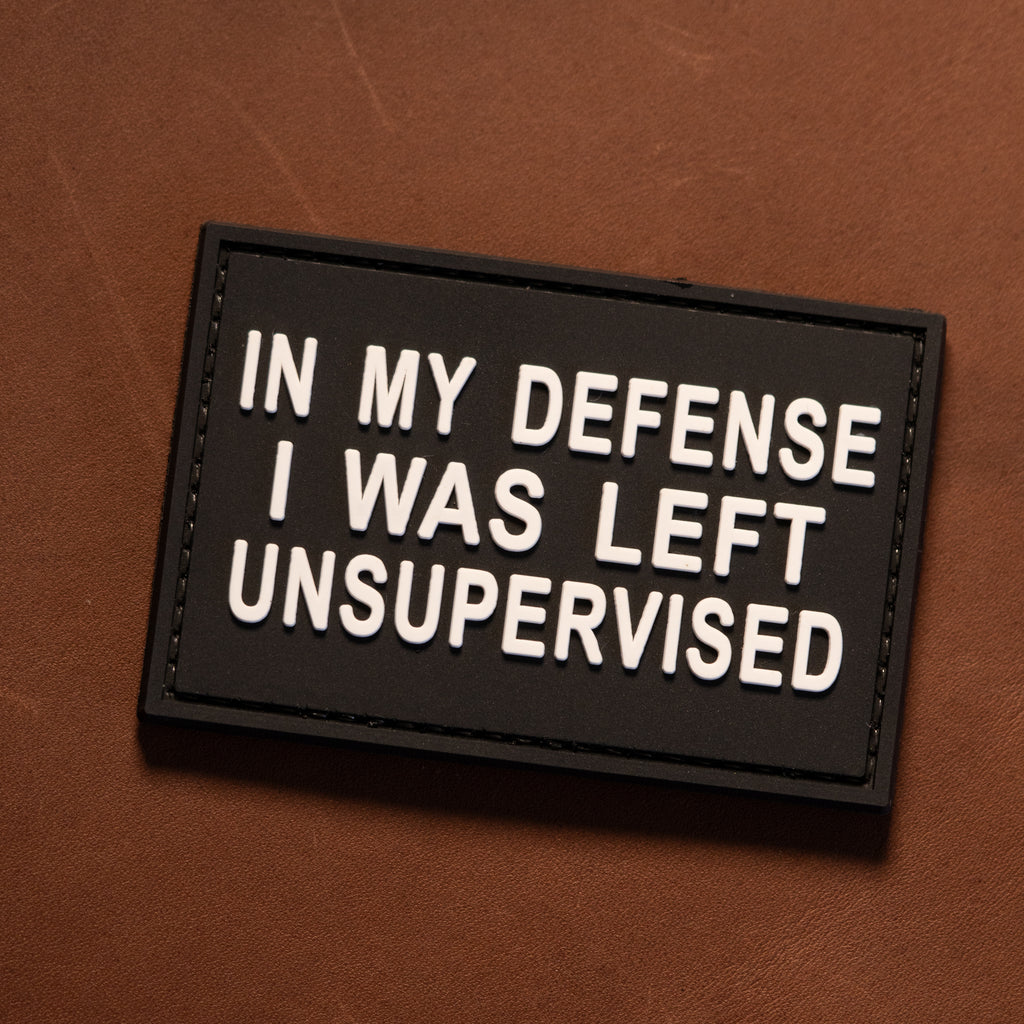 Left Unsupervised PVC morale patch with white quote text on black background