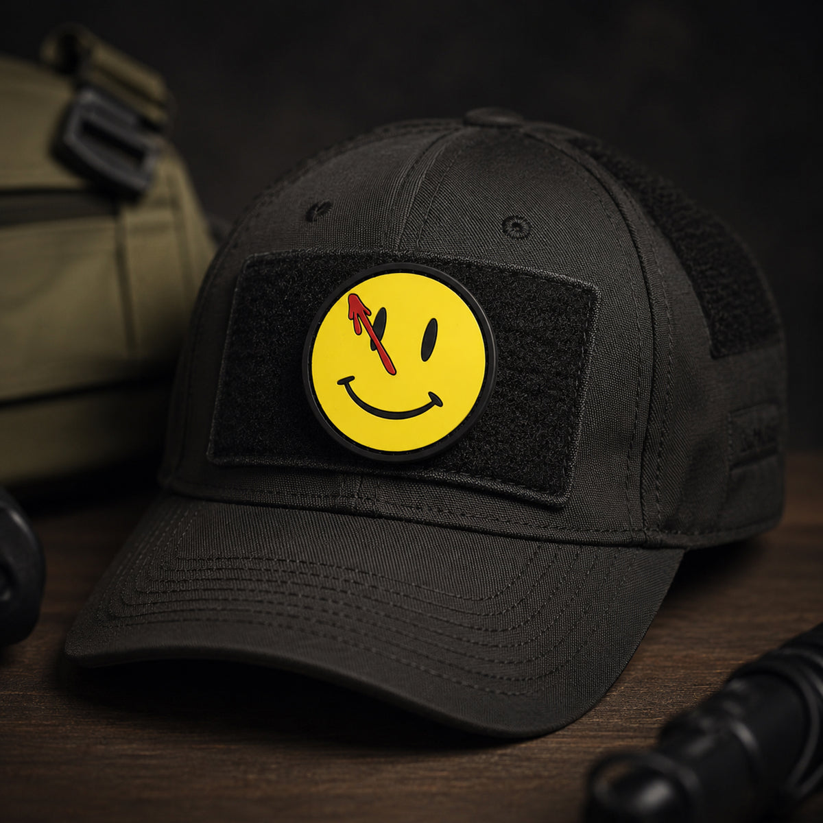 Watchmen PVC morale patch with yellow smiley face and red blood splatter attached to a black tactical cap